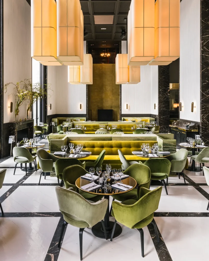 Art Deco dining room with green and yellow velvet seating, tall fabric pendants and a checkerboard floor at Monsieur Bleu Paris