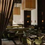 Green velvet chairs and marble tables beneath oversized fabric pendant lights and curtains at Monsieur Bleu Paris