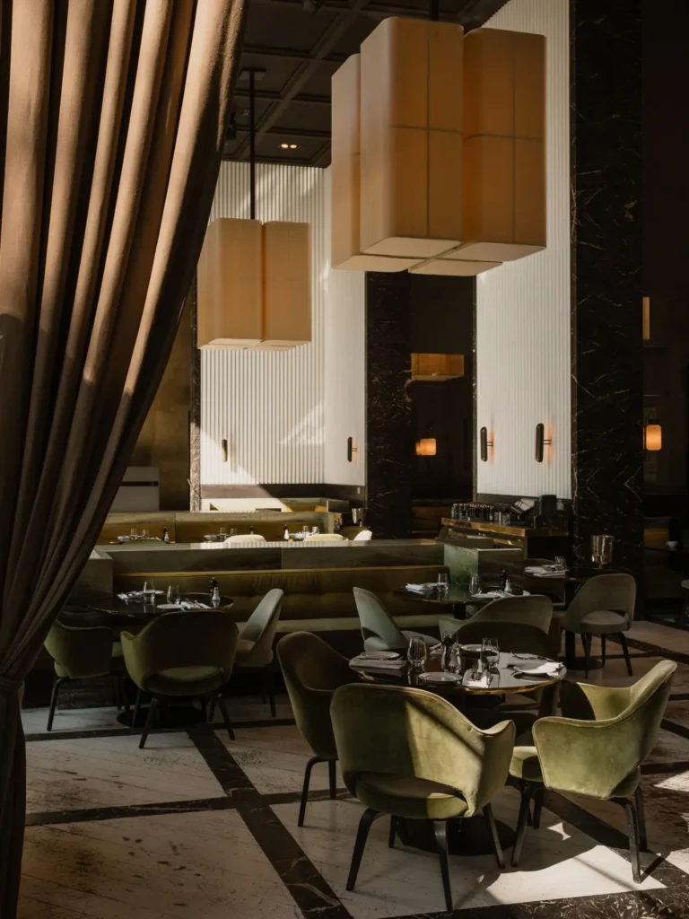 Green velvet chairs and marble tables beneath oversized fabric pendant lights and curtains at Monsieur Bleu Paris