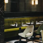 Green banquette and marble table below glass wall sconces on a checkerboard floor at Monsieur Bleu Paris