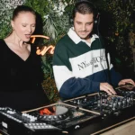 DJ and singer performing before a foliage wall with a neon sign at Monsieur Bleu Paris