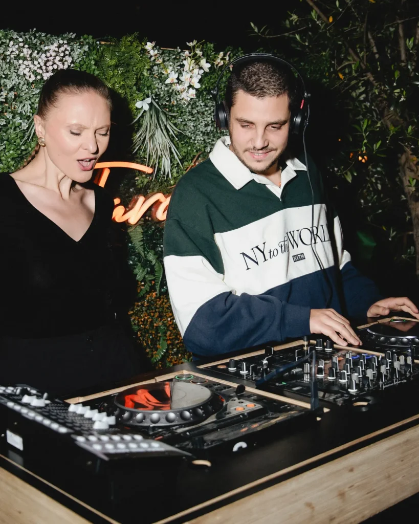 DJ and singer performing before a foliage wall with a neon sign at Monsieur Bleu Paris