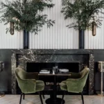 Green velvet chairs at a table set within a marble fireplace below tall olive branches at Monsieur Bleu Paris