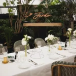 Long event table set before a Le Jardin neon sign and DJ booth in a greenery-filled space at Monsieur Bleu Paris