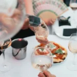 Rosé being poured over a margherita pizza as a guest holds a hand fan at Monsieur Bleu Paris