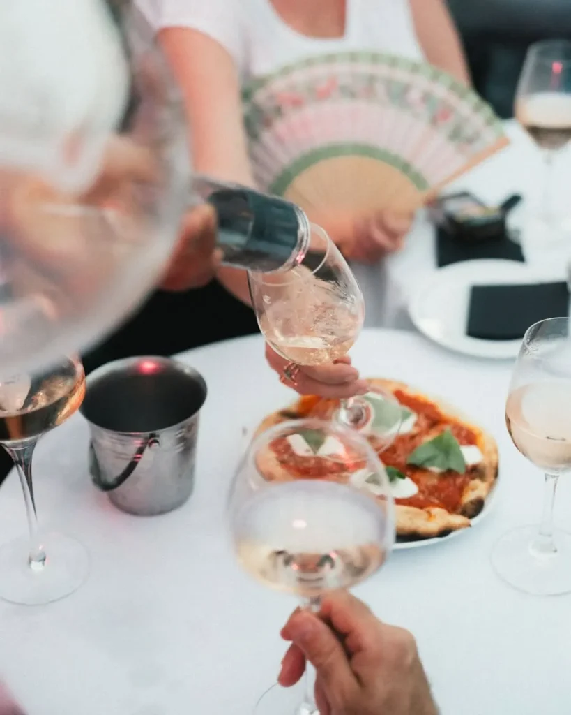 Rosé being poured over a margherita pizza as a guest holds a hand fan at Monsieur Bleu Paris