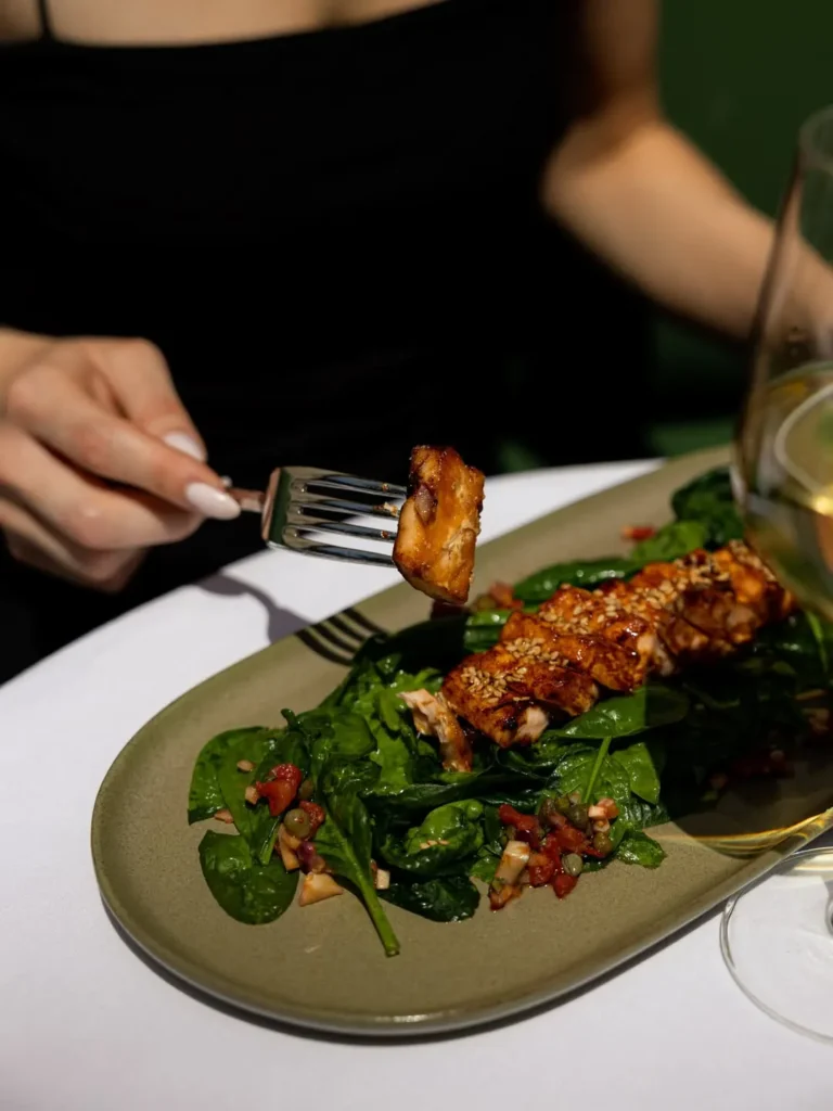 Glazed sesame salmon over spinach on a green plate with white wine at Monsieur Bleu Paris