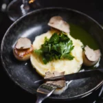 Seared scallops with mashed potato, herbs and shaved truffle in a black bowl at Monsieur Bleu Paris