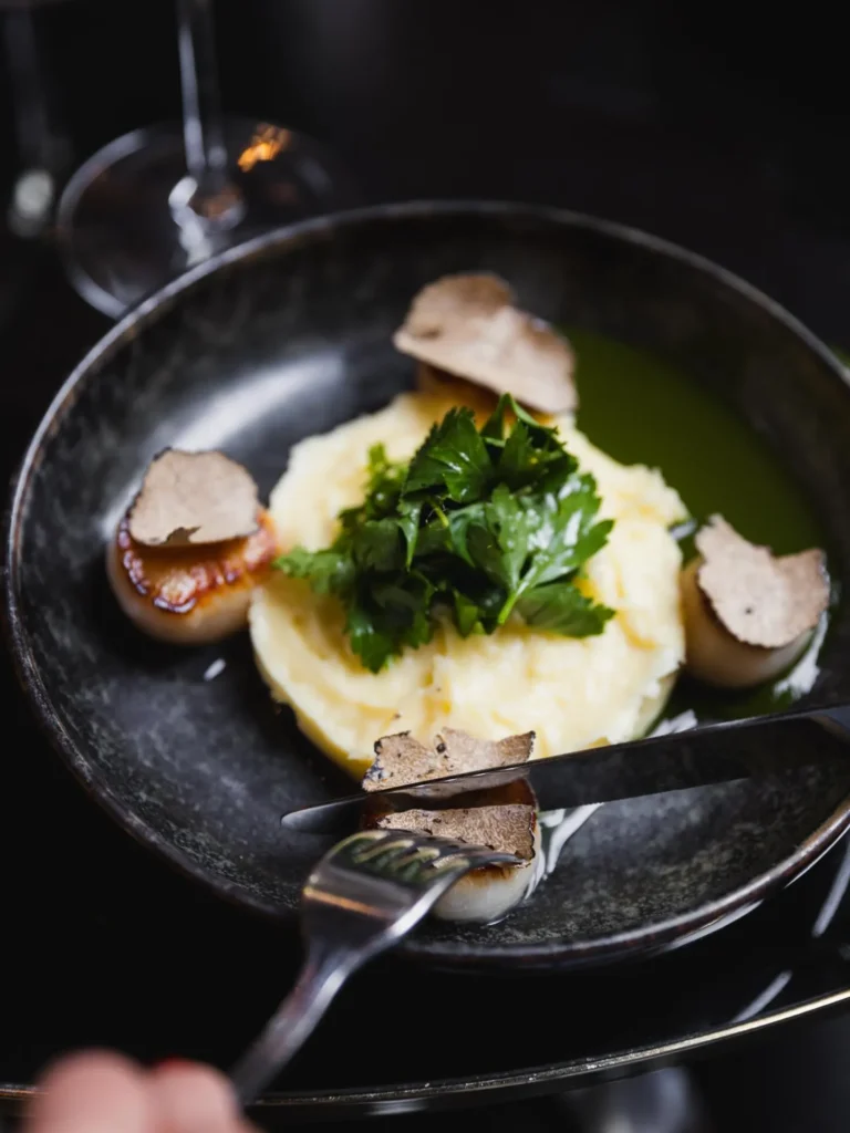 Seared scallops with mashed potato, herbs and shaved truffle in a black bowl at Monsieur Bleu Paris
