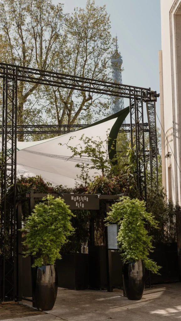 Monsieur Bleu sign above the planted entrance with the Eiffel Tower beyond the trees at Monsieur Bleu Paris