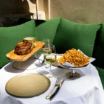 Grilled rib steak on a wooden board with a silver dish of fries on a terrace table at Monsieur Bleu Paris
