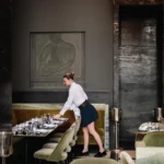 Server laying a banquette table beneath a carved stone relief at Monsieur Bleu Paris