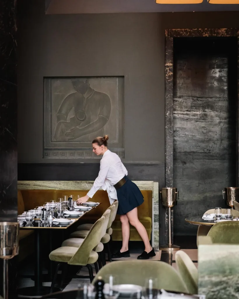 Server laying a banquette table beneath a carved stone relief at Monsieur Bleu Paris