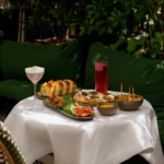 Truffle pizza, charcuterie, bread and cocktails on a terrace table by green cushions at Monsieur Bleu Paris