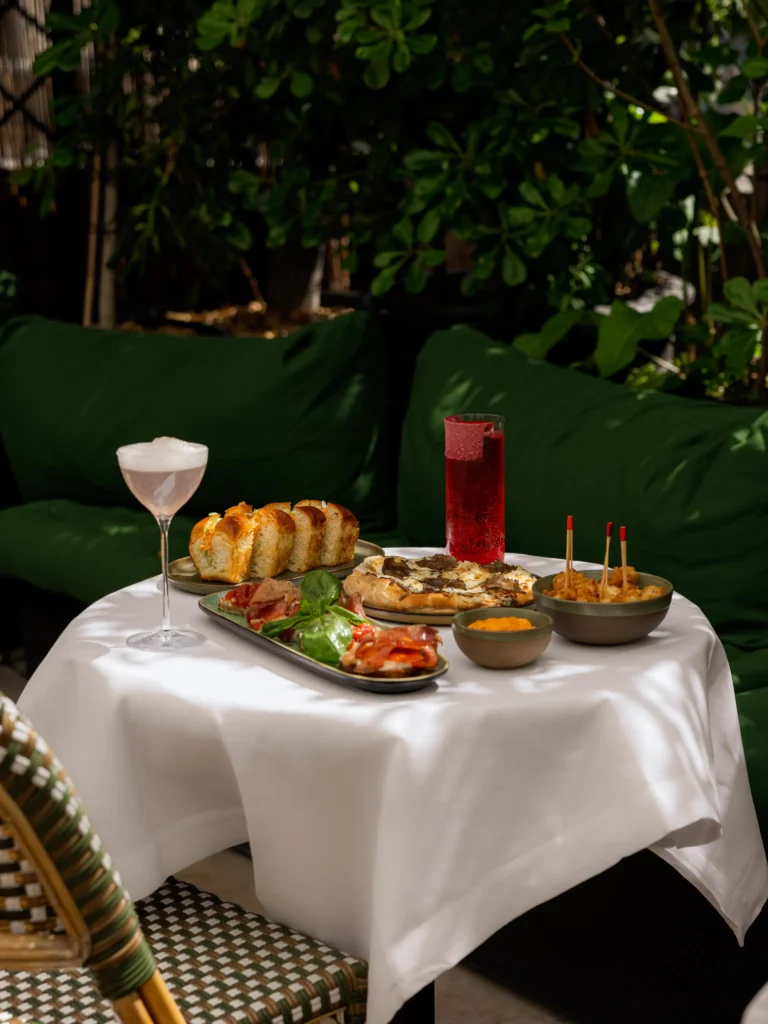 Truffle pizza, charcuterie, bread and cocktails on a terrace table by green cushions at Monsieur Bleu Paris