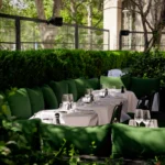 Green-cushioned terrace banquette and set tables framed by clipped hedges in daylight at Monsieur Bleu Paris