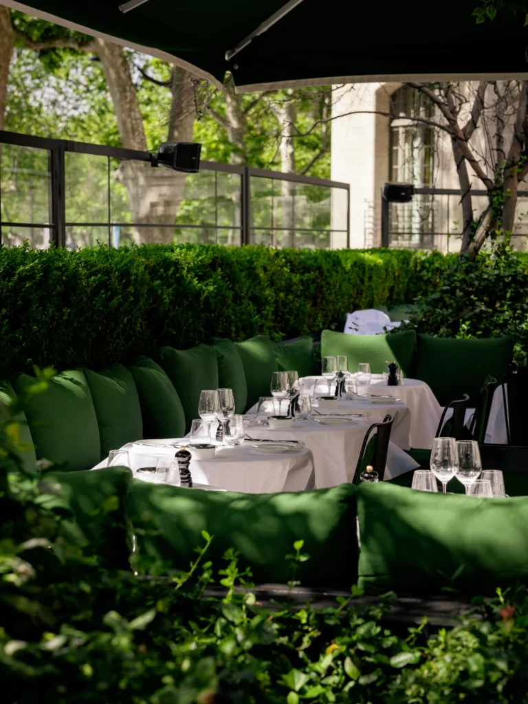 Green-cushioned terrace banquette and set tables framed by clipped hedges in daylight at Monsieur Bleu Paris