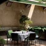 Round terrace table with green-cushioned chairs under heaters and a green awning at Monsieur Bleu Paris