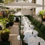 Row of white-clothed terrace tables along a green banquette with potted greenery at Monsieur Bleu Paris