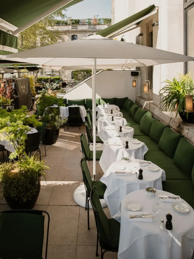 Row of white-clothed terrace tables along a green banquette with potted greenery at Monsieur Bleu Paris