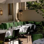 Sunlit terrace with green banquettes and set tables under a white parasol at Monsieur Bleu Paris