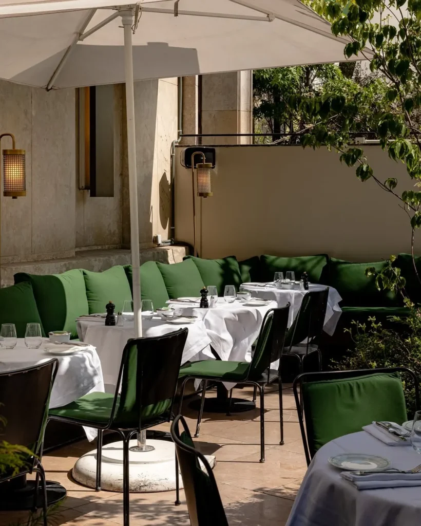 Sunlit terrace with green banquettes and set tables under a white parasol at Monsieur Bleu Paris