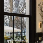 Tables by a tall window framing the Eiffel Tower with green velvet chairs at Monsieur Bleu Paris