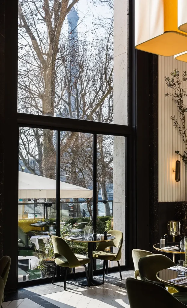 Tables by a tall window framing the Eiffel Tower with green velvet chairs at Monsieur Bleu Paris