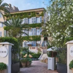View through the gate into the courtyard with the stone staircase and ivy facade at Monsieur Dior des Lices Saint-Tropez by Mauro Colagreco