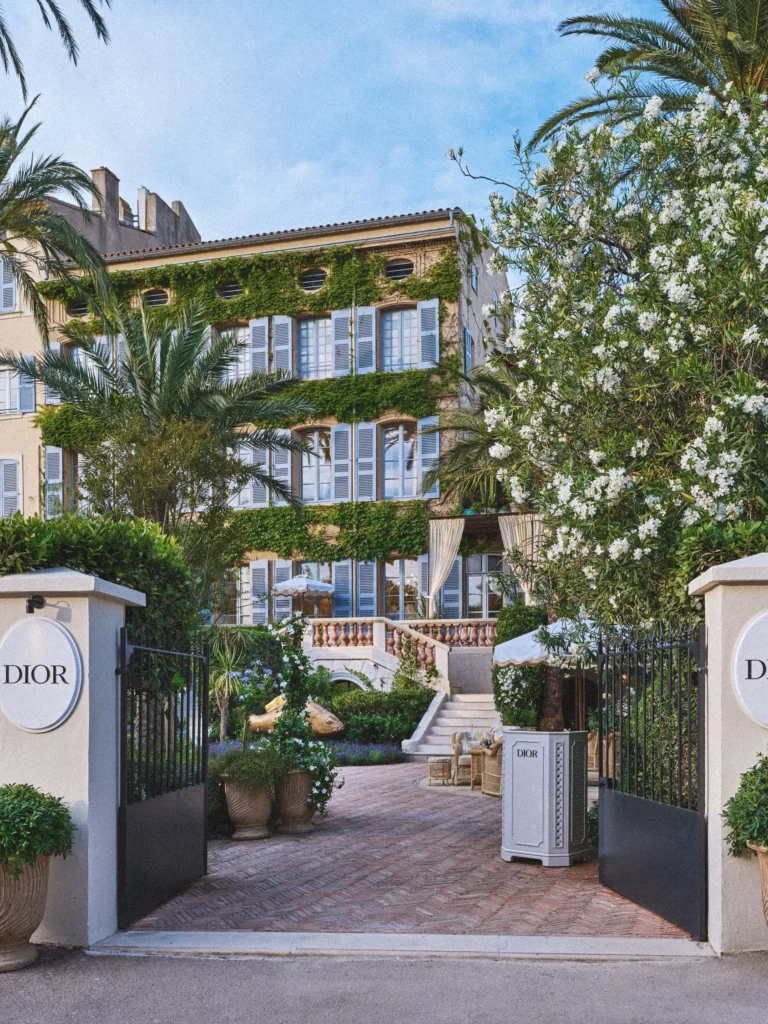 View through the gate into the courtyard with the stone staircase and ivy facade at Monsieur Dior des Lices Saint-Tropez by Mauro Colagreco