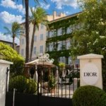 Iron gate with an oval DIOR sign and palm trees before the ivy-clad facade at Monsieur Dior des Lices Saint-Tropez by Mauro Colagreco
