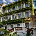 Ivy-clad facade with blue shutters and a balustraded staircase at Monsieur Dior des Lices Saint-Tropez by Mauro Colagreco