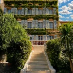 Ivy-covered facade with blue shutters above a stone staircase at Monsieur Dior des Lices Saint-Tropez by Mauro Colagreco