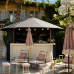 Outdoor bar with stools and pink fringed parasols under a palm at Monsieur Dior des Lices Saint-Tropez by Mauro Colagreco