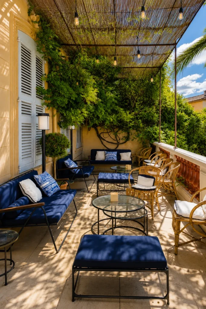 Covered terrace lounge with navy sofas and toile cushions under a vine-shaded pergola at Monsieur Dior des Lices Saint-Tropez by Mauro Colagreco