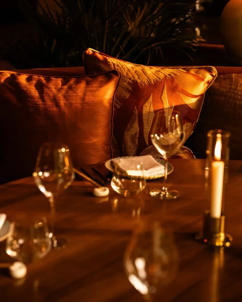 Candlelit table setting at NAŌ Saint-Tropez with wine glasses and silk cushions