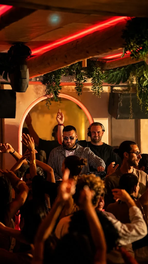 DJ performing to a lively crowd under an arched neon light at NAŌ Saint-Tropez