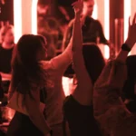 Guests dancing under red neon lighting during nightlife at NAŌ Saint-Tropez
