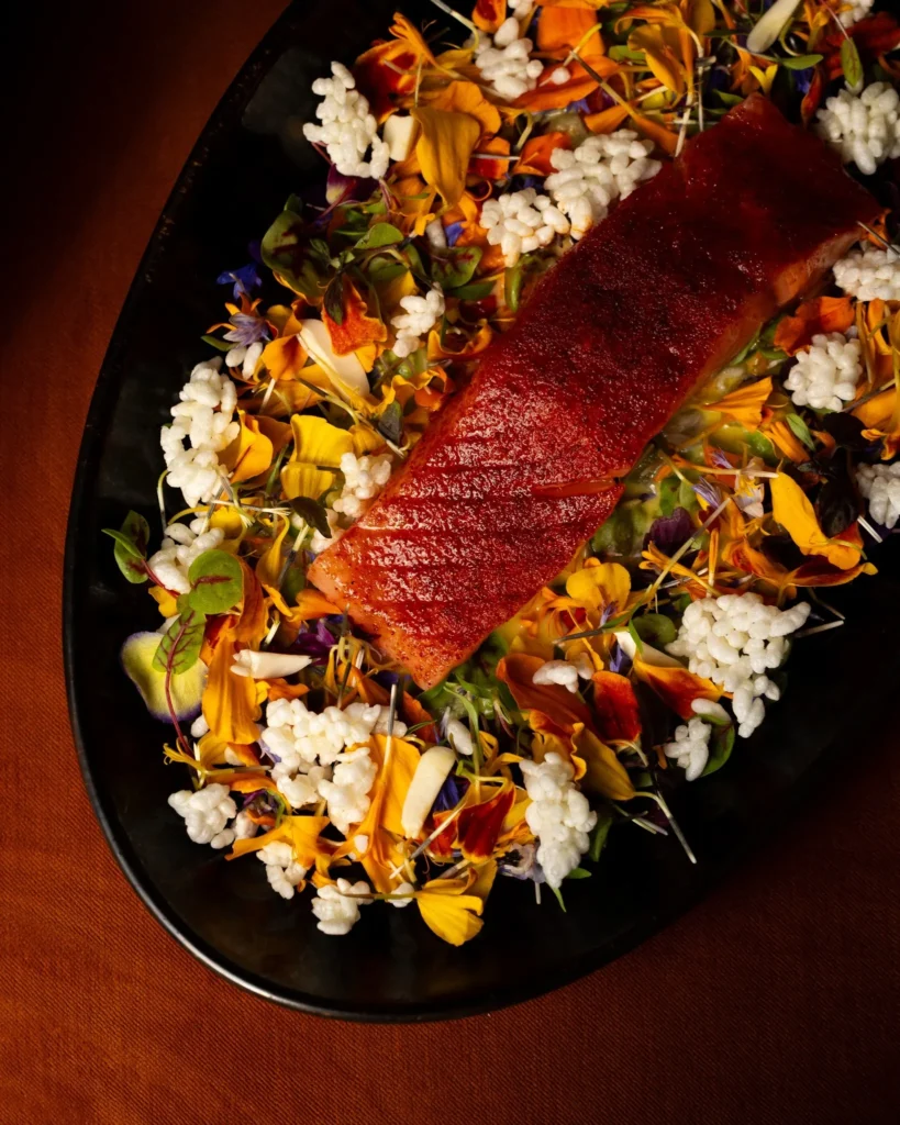 Glazed salmon dish garnished with edible flowers and puffed rice at NAŌ Saint-Tropez
