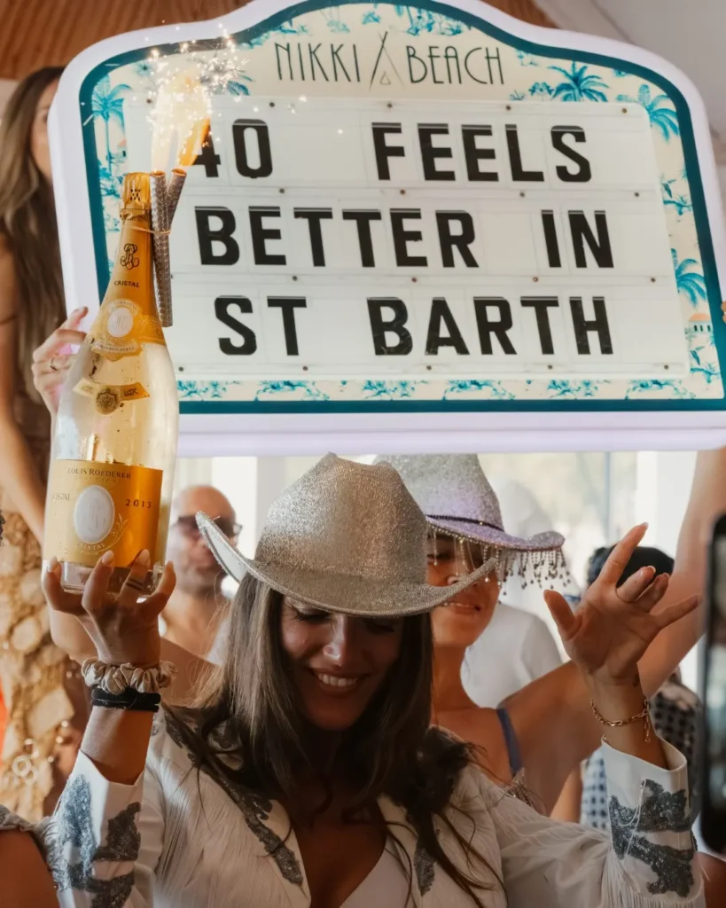 Guest holding a sparkler-topped champagne bottle beneath a Nikki Beach letter-board sign at Nikki Beach Saint Barth