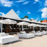 White daybeds and branded parasols in front of the beachfront restaurant at Nikki Beach Saint Barth