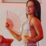 Guest with a hand fan and a glass of champagne at Nikki Beach Saint Barth