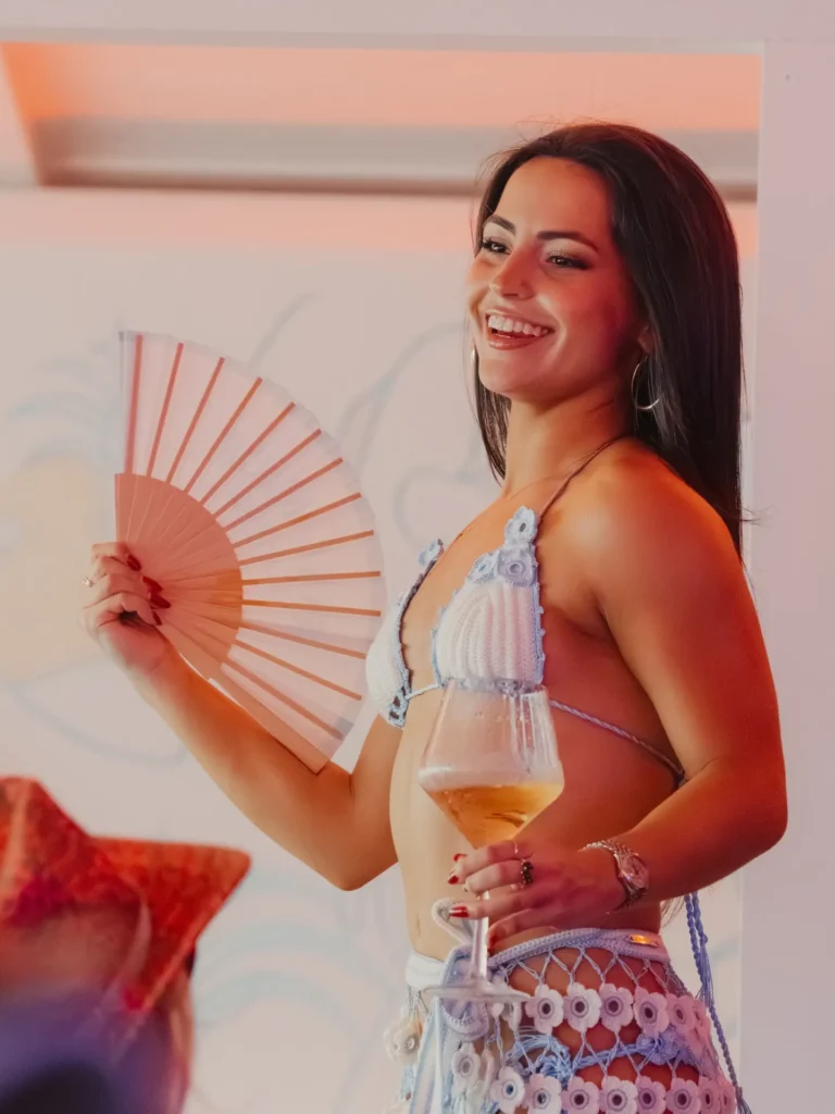 Guest with a hand fan and a glass of champagne at Nikki Beach Saint Barth