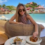 Guest on a woven daybed with plated dishes overlooking the bay at Nikki Beach Saint Barth