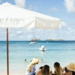 Guests on a daybed under a Nikki Beach parasol looking out to boats and islets at Nikki Beach Saint Barth