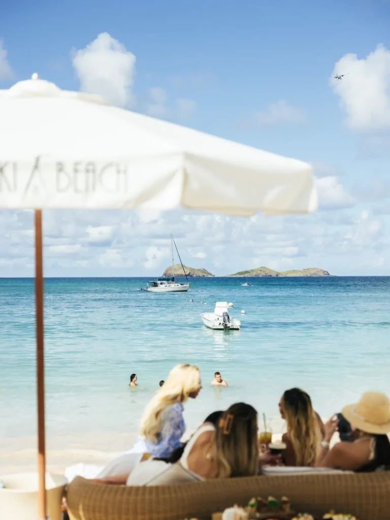 Guests on a daybed under a Nikki Beach parasol looking out to boats and islets at Nikki Beach Saint Barth