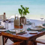 Wooden table set with shell placemats and a potted plant beside the sea at Nikki Beach Saint Barth