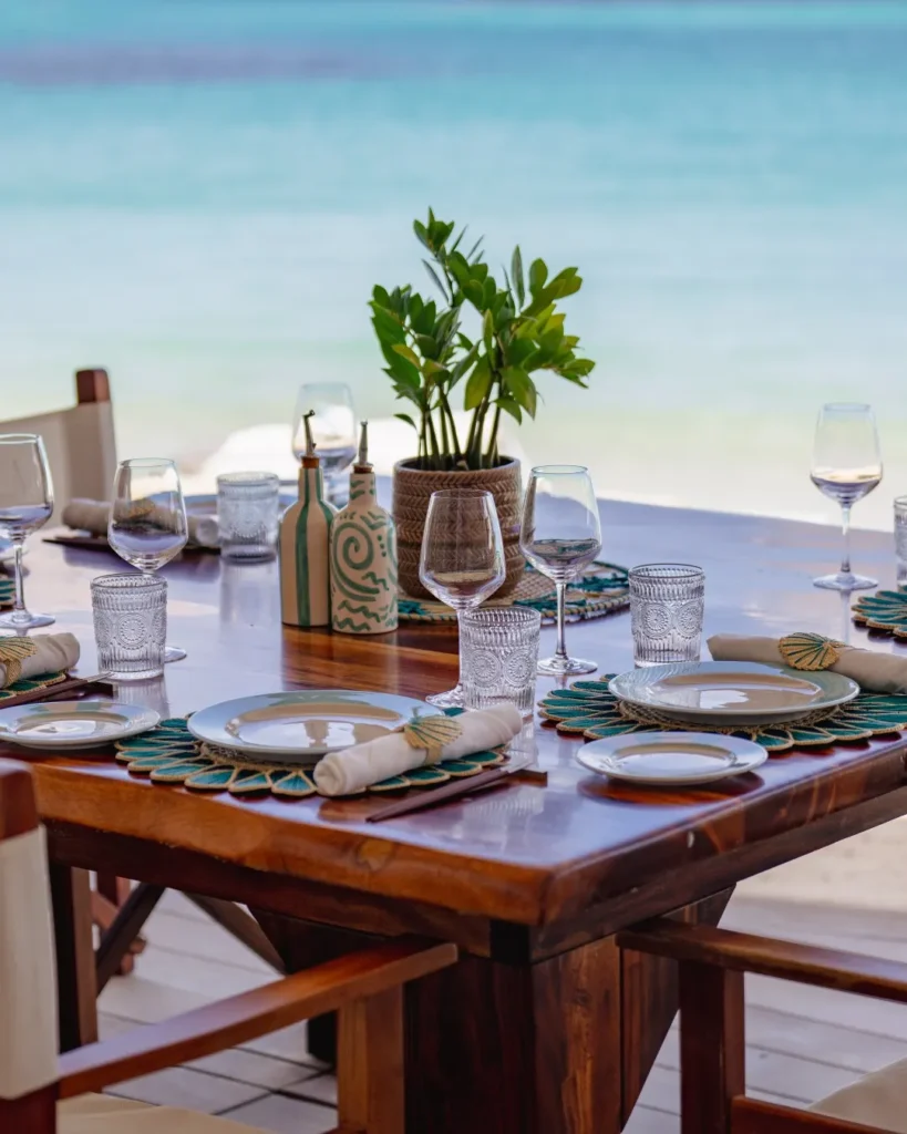 Wooden table set with shell placemats and a potted plant beside the sea at Nikki Beach Saint Barth