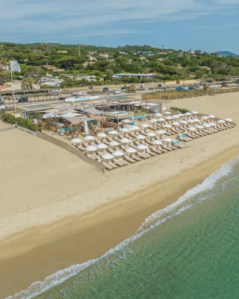 Aerial view of the beach club with sunbeds and the La Serena sign on the shore at Plage La Serena Ramatuelle Saint-Tropez