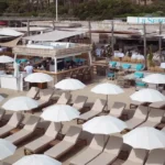 Elevated view of the bar, sunbeds and white parasols with the La Serena flag at Plage La Serena Ramatuelle Saint-Tropez